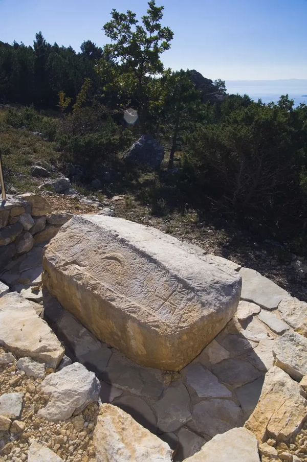 Nadgrobni spomenik stećak na Grebišću jugoistočno od sela Bast, koji pripada pločastoj vrsti sljemenjaka, ukrašen polumjesecom i svastikama (Izvor: Baška Voda (baskavoda.hr))