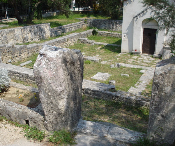 Dva nadgrobna kamena s napuštenoga groblja uz crkvu Sveti Juraj (Jure) u Tučepima, koji su izmješteni i uspravljeni da služe kao vratnice (Foto: Silverije, 2013.; Izvor: Wikipedia (wikipedia.org))